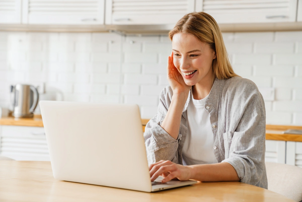 Elena Janice smiling while working on her laptop in a bright kitchen, developing Mediterranean recipes for DashOfFlavor.