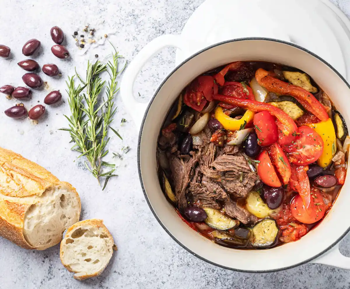 Mediterranean roast beef pot with olives, tomatoes, and herbs in a Dutch oven
