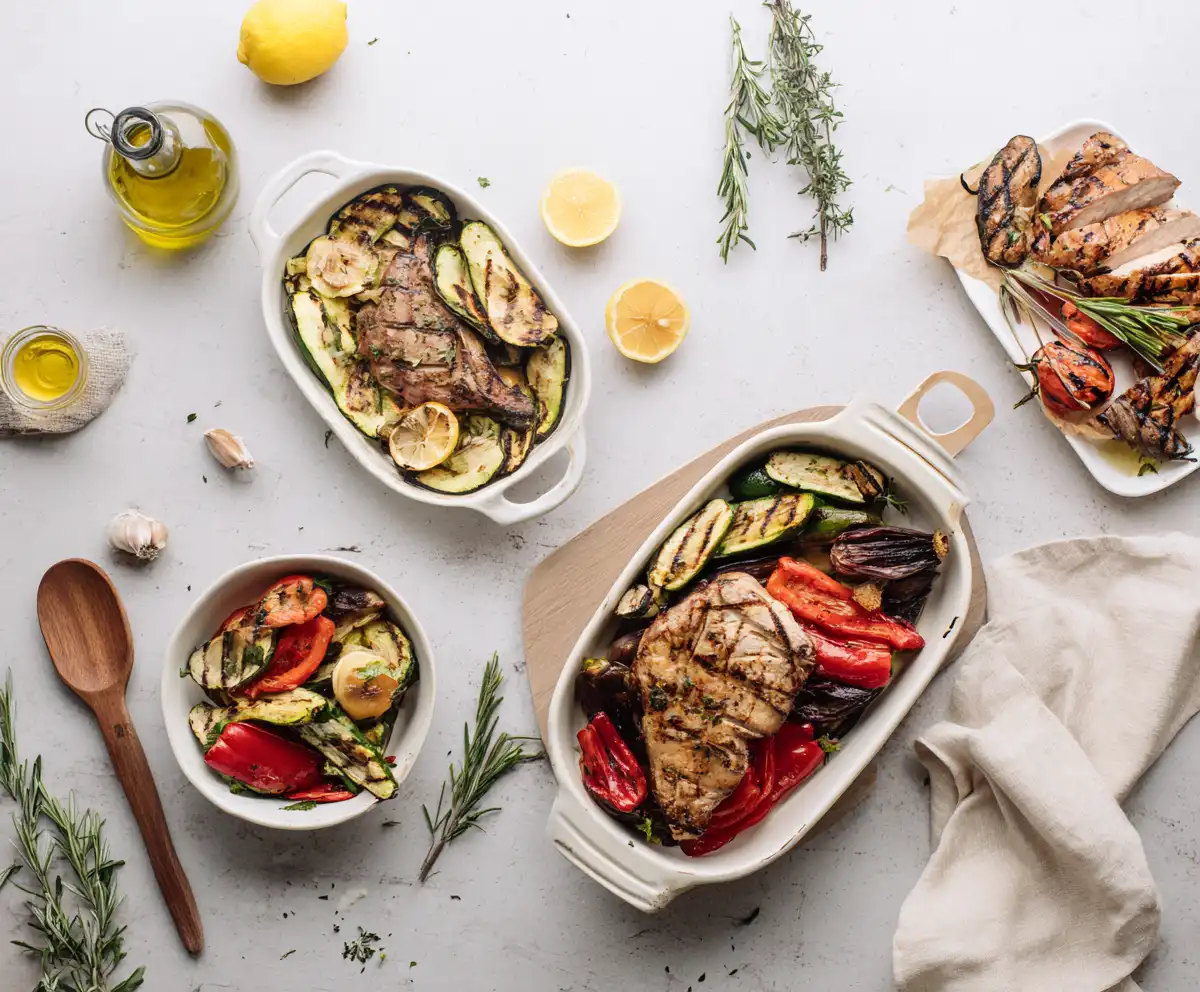 Mediterranean roast dinner spread with grilled meats, vegetables, olive oil, and lemon halves on a white table