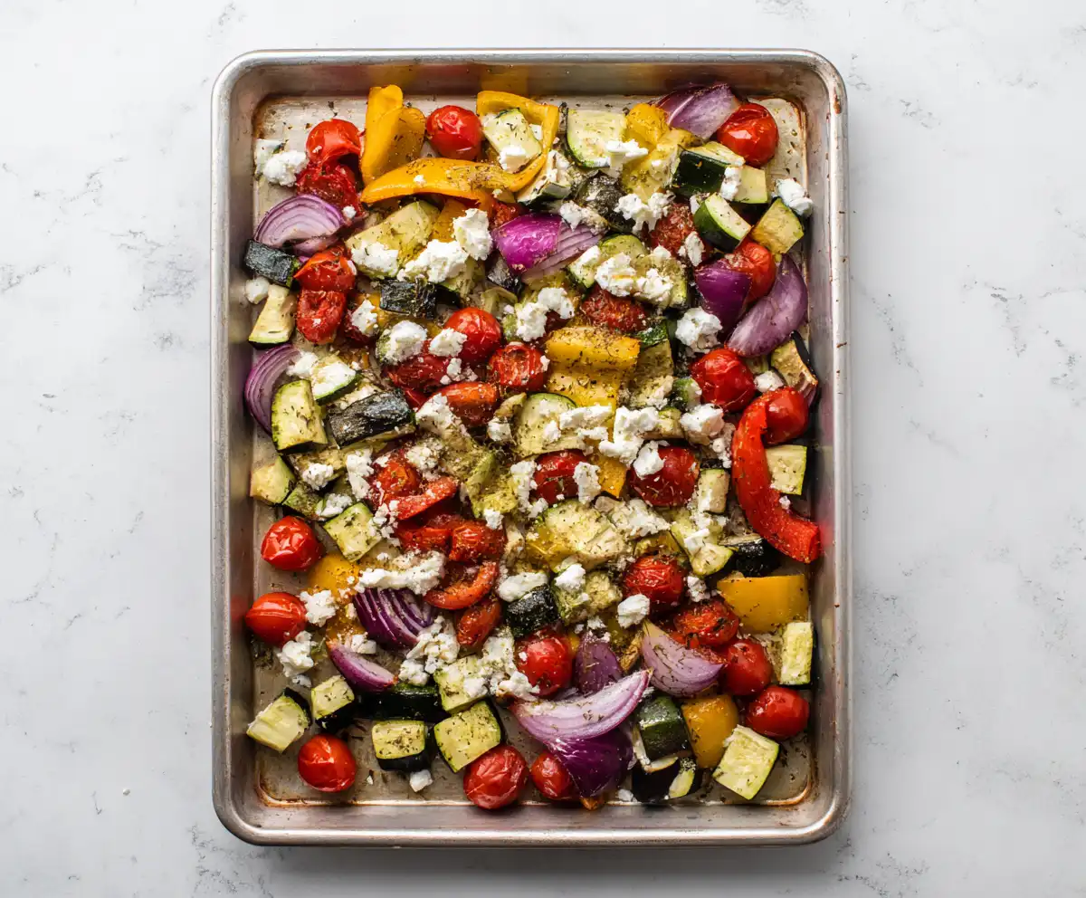 Mediterranean roasted vegetables with feta cheese, zucchini, bell peppers, and cherry tomatoes on a baking tray