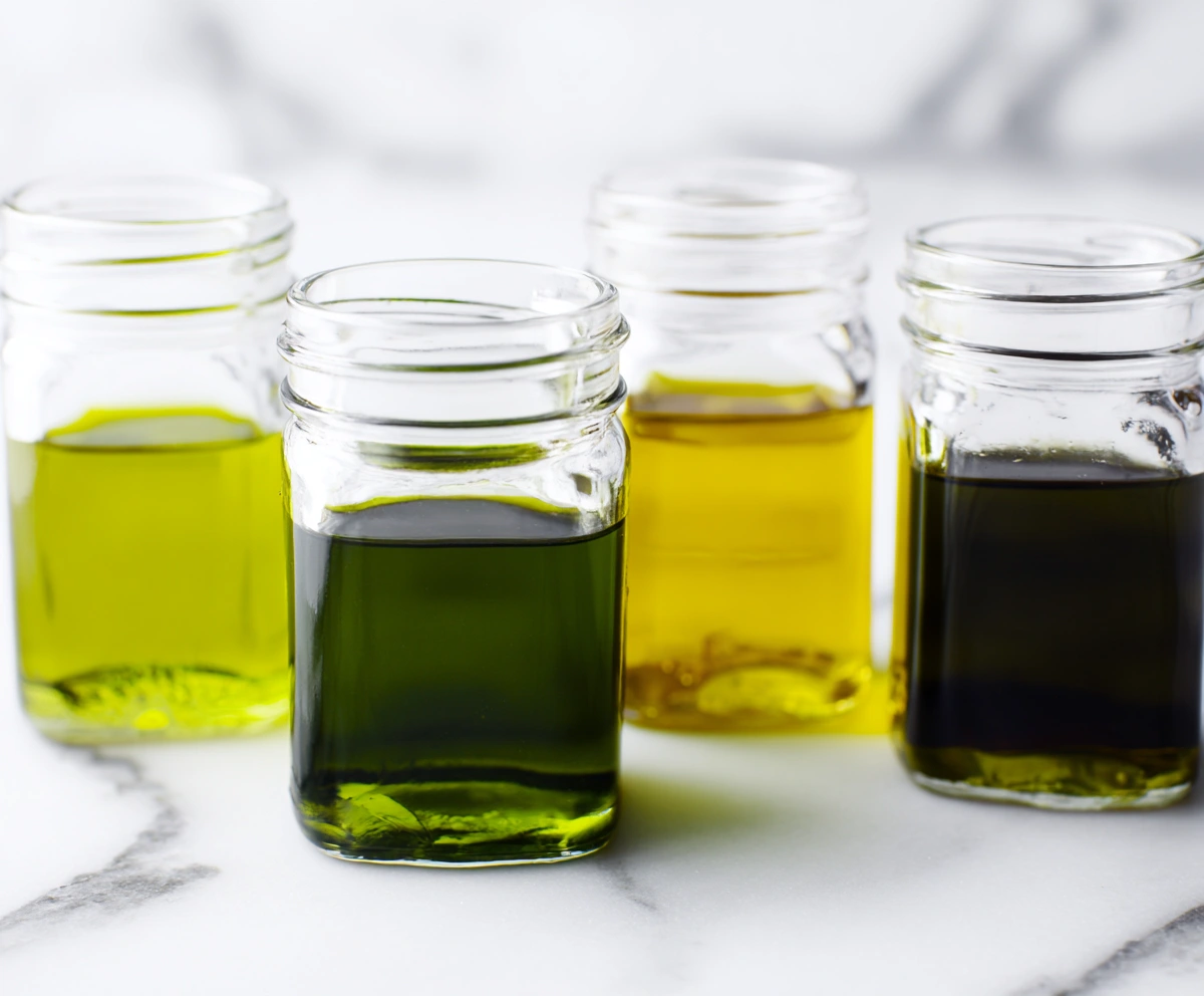four glass jars showing different colors of types of olive oil on white stone four glass jars showing different colors of types of olive oil on white stone